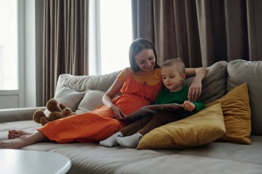 Gencecik bir çocuğun resimlere bakıp hikayenin tadını çıkardığı gülümseyen bir anne kitabı.