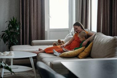 Oturma odasındaki büyük koltukta rahatlarken hamile kadın ve oğlunun kitap okuması geniş açılı bir bakış açısı.