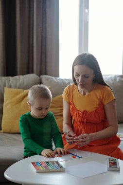 Hamile kadın ve küçük çocuğun dikey portresi el sanatları yapmaktan ve kille oynamaktan zevk alıyor.