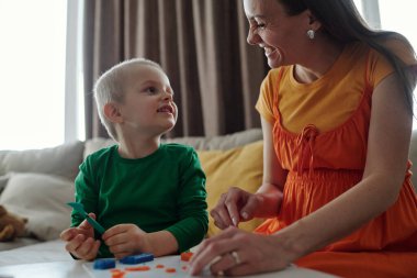 Gülümseyen anne ve oğlunun el sanatları yaptığı gizli bir sahne. Masada birbirlerine bakıyorlar.