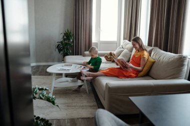 Anne oturma odasında kitap okurken, çocuk kil şekillerle oynuyordu.