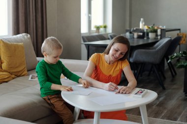 Oğluyla resim çizen gülümseyen genç bir annenin portresi ve kapalı alandaki sanatsal aktivitelerden zevk alıyor.