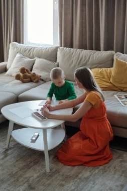 Anne ve oğlunun rahat bir ev sahnesinde birlikte resim çizdiği ve kapalı alanda sanatsal faaliyetlerin keyfini çıkardığı yüksek açılı manzara.