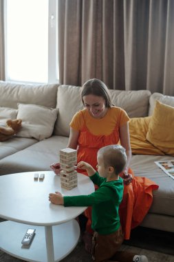 Anne ve oğlunun dikey portresi dikkatli bir şekilde ahşap blok kulesi inşa ediyor ve ev aktivitelerinin keyfini çıkarıyor.