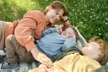Mutlu aile anne ve iki çocuğun piknik battaniyesinde uzandığı ve neşeyle gülümsediği gizli bir sahne. 