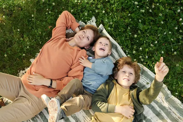 Anne ve iki çocuğun piknik battaniyesinde uzanmış hayal kurarken gökyüzüne ve bulutlara bakarken. 