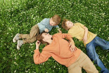 Yeşil çimlerde uzanan iki çocukla birlikte doğanın tadını çıkaran anne manzarası, kopyalama alanı.