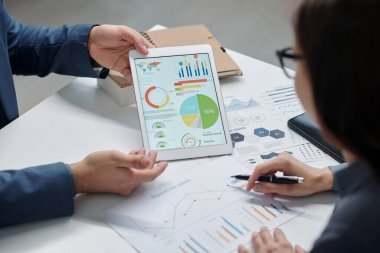 Ofis fotokopi alanındaki toplantı sırasında tablet ekranında veri istatistiklerini tartışan tanınmayan iki meslektaşın yüksek açılı yakın çekimi