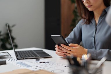 İş yerinde fotokopi odasında otururken akıllı telefon kullanan iş kadınını kapat