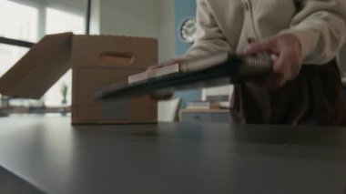 Emeklilik gününde ofisini toplarken siyah klasörleri karton kutuya koyan tanınmayan yaşlı bir kadının görüntüsü.