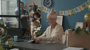 Yaşlı beyaz kadın, işle ilgili eşyalarını karton kutuya koyuyor. Ofis emeklilik partisindeki iş arkadaşlarının hediyeleriyle ve kekiyle sevinçle şaşırıyor. Etrafı gülücükler ve alkışlarla dolu.