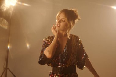 Stüdyoda klip çekimi sırasında dramatik ışıklandırma altında performans gösteren genç bir kadının belden yukarı portresi.