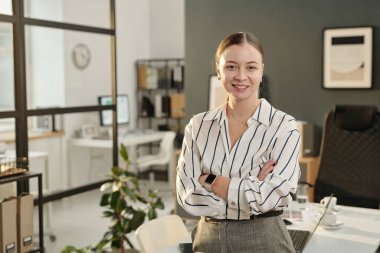 Modern ofiste kolları çapraz duran ve kameraya gülümseyen, fotokopi çeken kendine güvenen genç iş kadınının belini kaldırın.