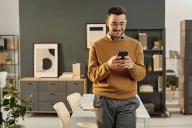 Ofiste durup internet üzerinden mesajları kontrol eden gülümseyen genç bir adamın ön görünüm portresi, boşluğu kopyala