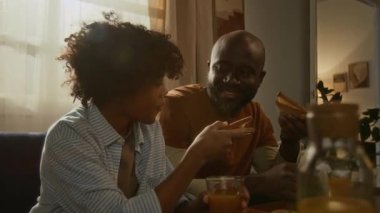 Afrika kökenli Amerikalı kökenli baba ve oğul güneşli oturma odalarında sıcak bir şekilde sandviçlerini, portakal sularını ve sohbetlerini paylaşıyorlar.