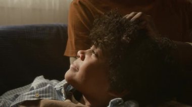 Afrikalı Amerikalı babanın parmaklarını oğlunun buklelerinde gezdirmesi, altın güneş ışığında huzur içinde dinlenmesi, sıcaklık ve sessiz aşkla çevrili.