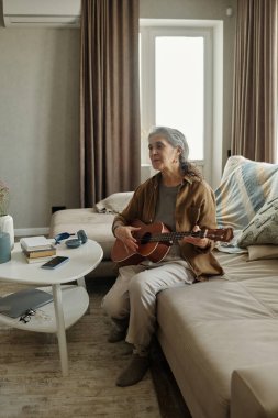 Oturma odasındaki kanepede oturan son sınıf öğrencisi gitar tıngırdatıyor. Yakınındaki masaya çeşitli ögeler yerleştirilmiş çevre aydınlatma alanı