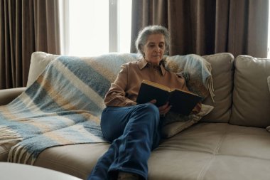 Kucağında battaniyeyle kanepede oturan gri saçlı yaşlı bir kadın.