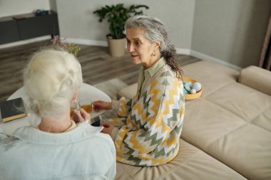 Kanepede oturan son sınıf kadınları modern oturma odasında sohbet ediyorlar. İçkileri ellerinde tutuyorlar ve sıcak ve samimi bir ortam yaratıyorlar.