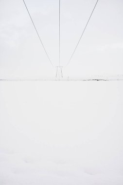 Elektrik kabloları, kışın kırsal kesimde soğuk gri bir günde karlı arazide uzak elektrik direklerine çıkıyor.