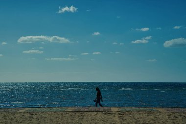 Güneşli bir günde sahilde yürüyen bir adam.