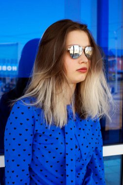 Genç bir kız bir süpermarketin mavi penceresinin önünde duruyor.