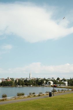 Yeşil sahil kaldırımlı yürüyüş yolu ve bulutlu gökyüzünün altında şehrin beyaz binaları.