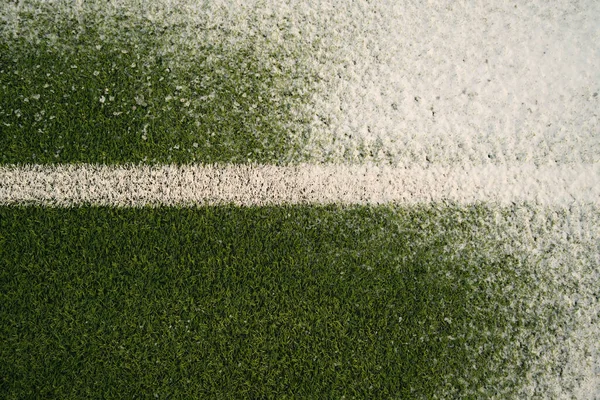Top view of grassy football pitch with white line covered with fresh snow on cold winter day
