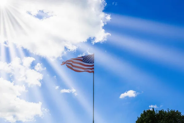 American flag waving in a cloudy sky and sunbeams. USA flag flies.