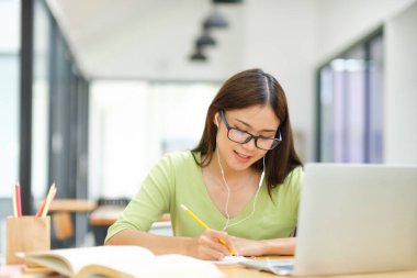 Genç Asyalı kız öğrenci evde bilgisayar kullanarak ve internetten öğrenerek okuyor. Evde dizüstü bilgisayarla iş dünyası bağımsız video konferansı.