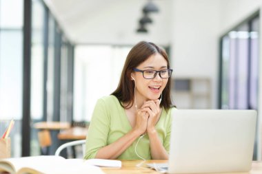 Genç Asyalı kız öğrenci evde bilgisayar kullanarak ve internetten öğrenerek okuyor. Evde dizüstü bilgisayarla iş dünyası bağımsız video konferansı.