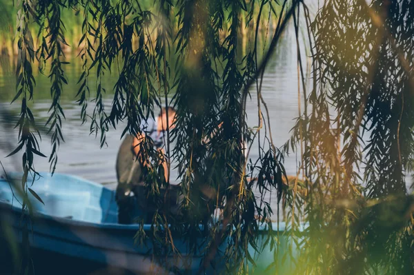 ハンギング ウィローの枝の後ろのボートで輝かしい漁師 — ストック写真