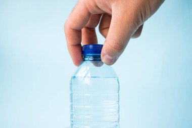 Mavi arka planda plastik su şişesini alan el.