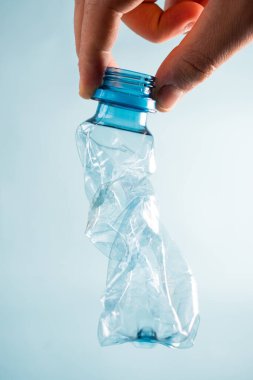 Mavi arka planda plastik şişeyi alan el.