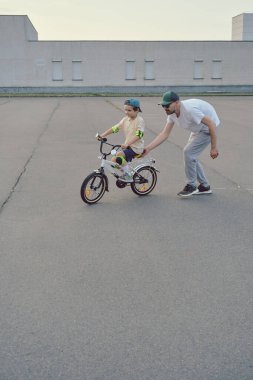 Baba oğlunun bisiklete binmesine yardım et.