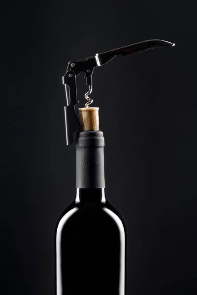 Corkscrew opening bottle of wine on dark background