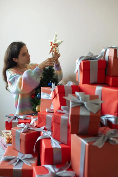 前面有很多红色的节日礼品盒 在背景中 一个女孩把一颗圣诞星挂在圣诞树上 — 图库照片