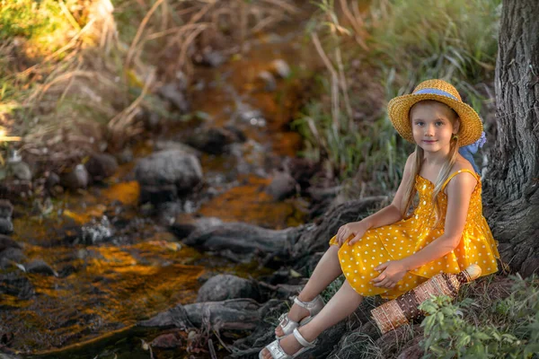 girl in a yellow dress sits by the stream