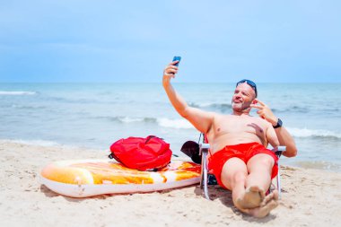 Kel adam yüzer, gezer, banyo yapar ve sahilde selfie çeker.