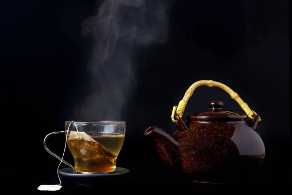 steaming tea cup with ceramic teapot insulated on black background
