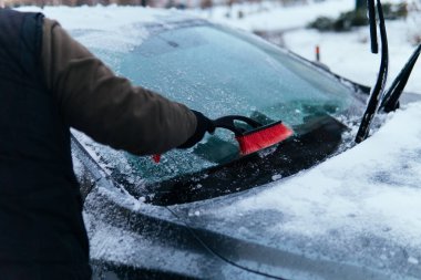 warmly dressed man cleans the car from snow and ice in winter