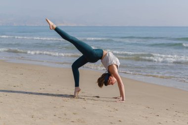 Genç kadın plajda yoga yapıyor.