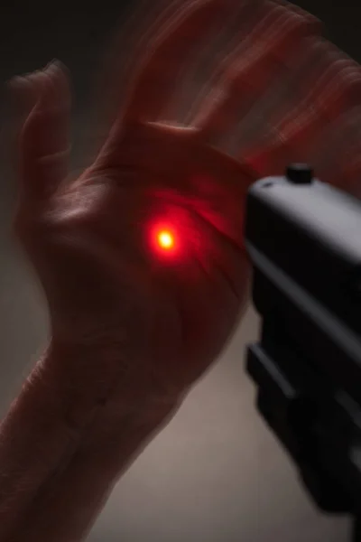 Expressive hands in front of a pistol with a laser gunsight