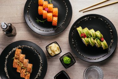Masadaki tabaklarda çeşitli suşi çeşitleri var. Soya sosu, wasabi. Asya restoranı menüsü