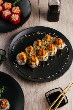 Masadaki tabaklarda çeşitli suşi çeşitleri var. Soya sosu, wasabi. Asya restoranı menüsü
