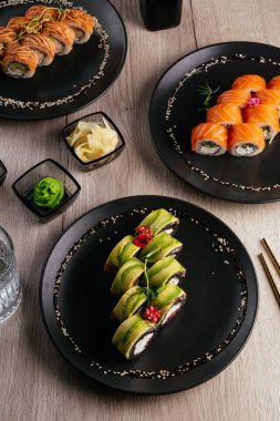Masadaki tabaklarda çeşitli suşi çeşitleri var. Soya sosu, wasabi. Asya restoranı menüsü