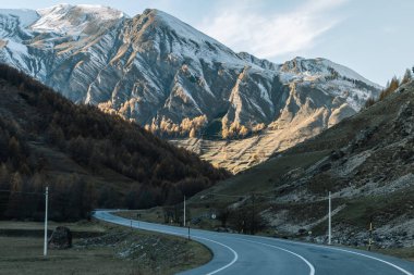 Güneşli bir günde karlı dağlarda asfalt yolu manzaralı.