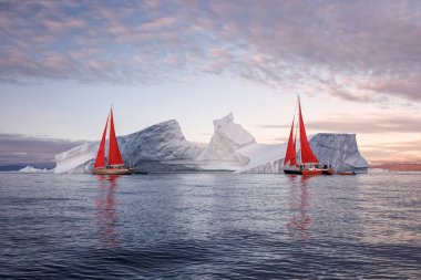 sailboats with red sails sailing between huge icebergs clipart