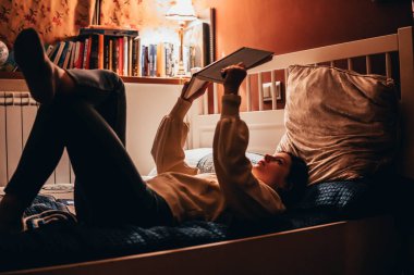 woman reading a book lying in bed at night