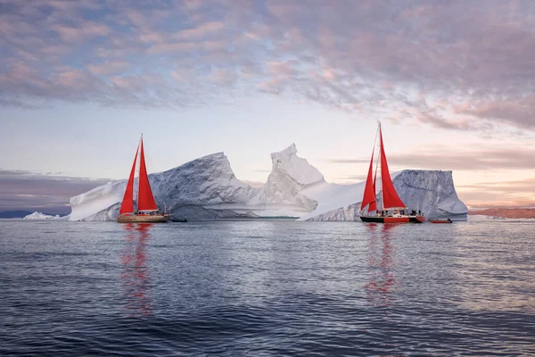 Kırmızı yelkenli yelkenliler büyük buzdağları arasında süzülüyor